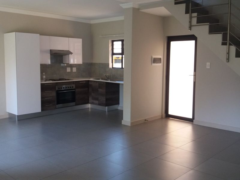 Open plan living area featuring a modern kitchen with built-in appliances, tiled flooring, and a staircase with stainless steel railings.