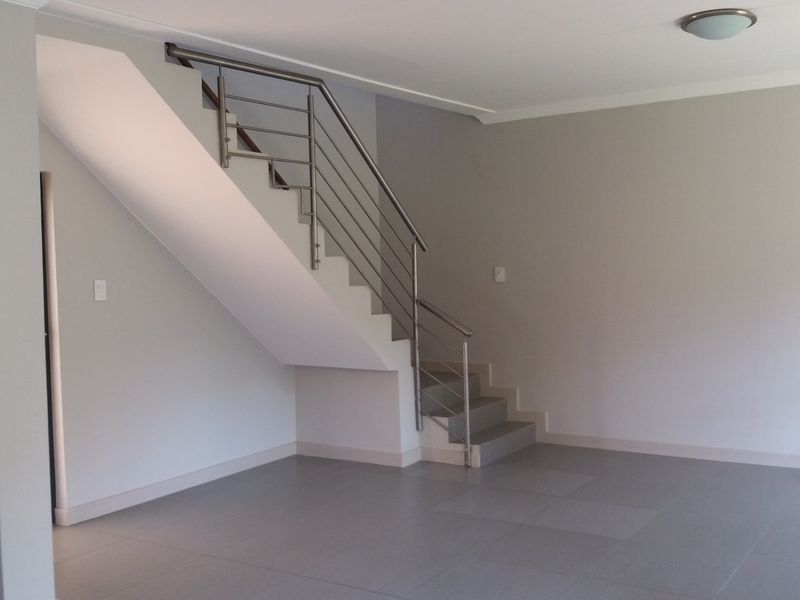 An open-plan living area featuring neutral tiled flooring, a modern staircase with a stainless steel balustrade, and clean, freshly painted walls.