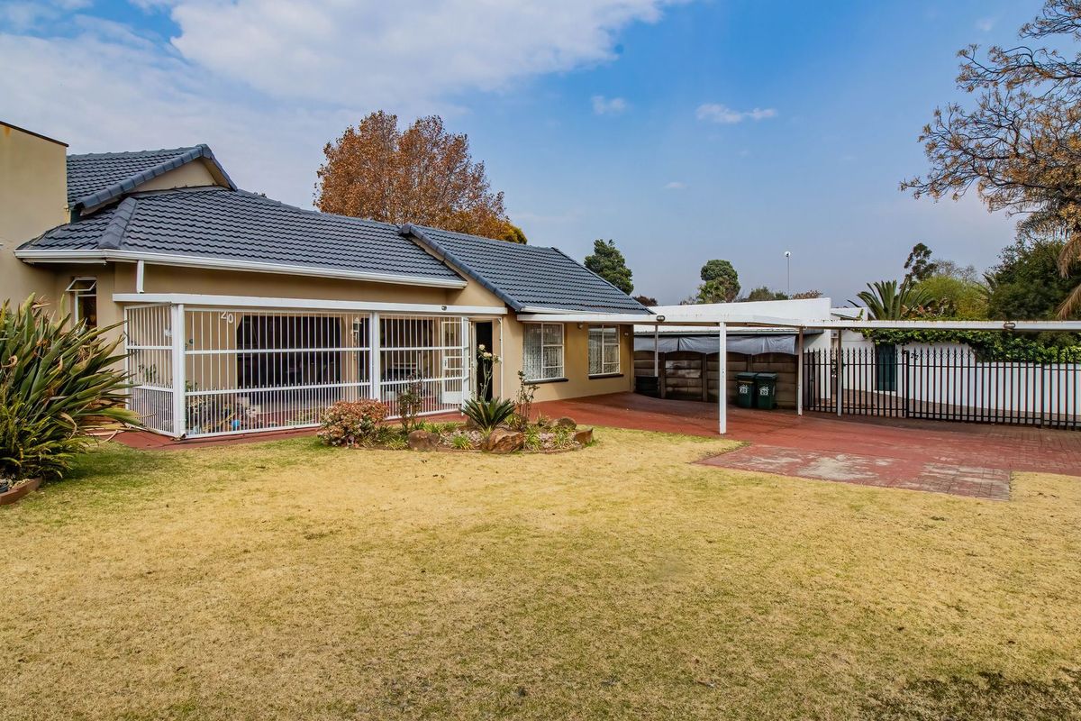 Rear view of the property featuring a tiled roof, paved driveway, carport, and secure perimeter fencing with a lawn area.