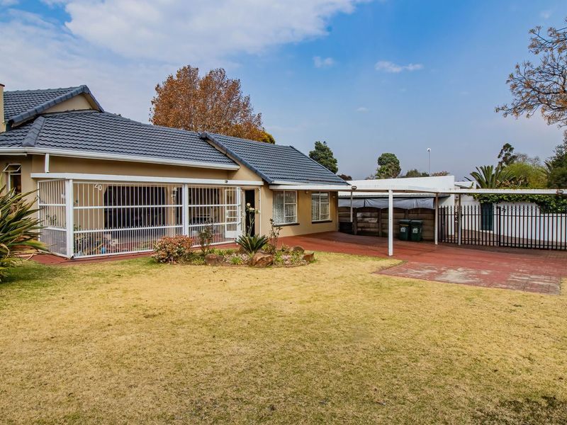 Rear view of the property featuring a tiled roof, paved driveway, carport, and secure perimeter fencing with a lawn area.