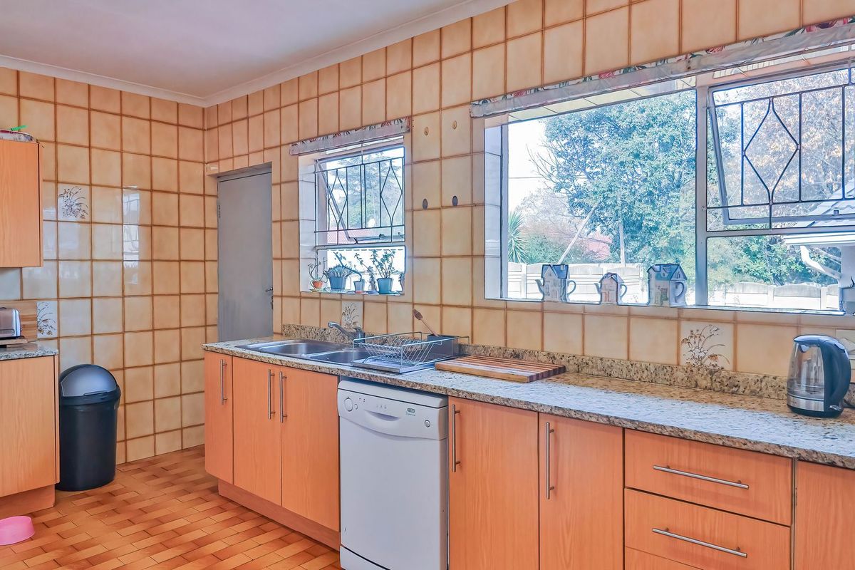 A functional kitchen featuring laminate cabinetry, granite countertops, a double bowl sink, and extensive wall tiling with security-fitted windows.