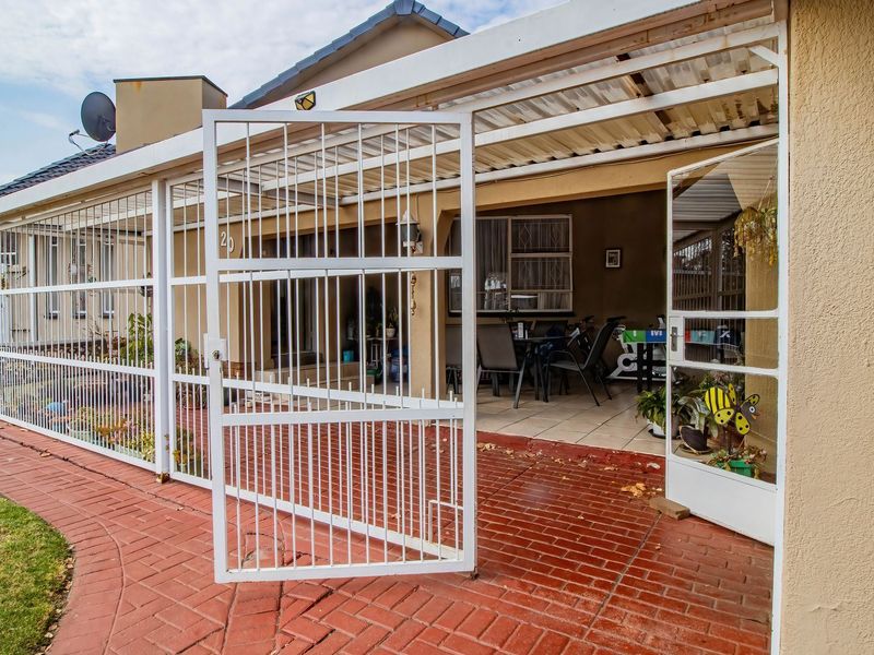 A covered patio area featuring brick paving, a security gate enclosure, and a corrugated roof structure, providing a functional outdoor living space.