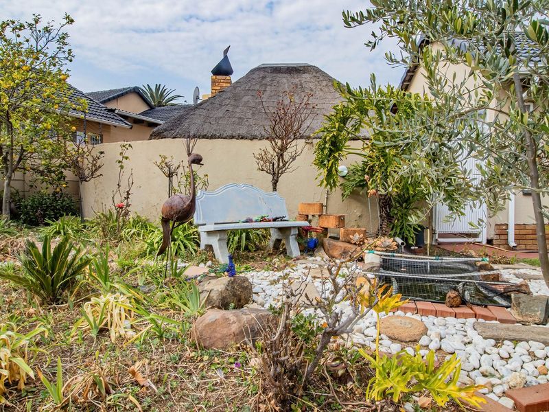 A landscaped garden area featuring a small water feature, stone pathways, and a view of a thatched roof structure with a brick boundary wall.