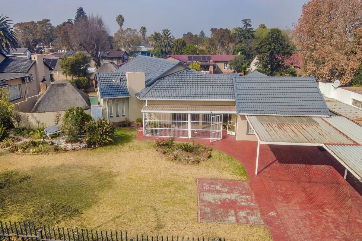 Aerial view of the property featuring a tiled roof, covered patio, carport, and a spacious garden with paved driveway areas.