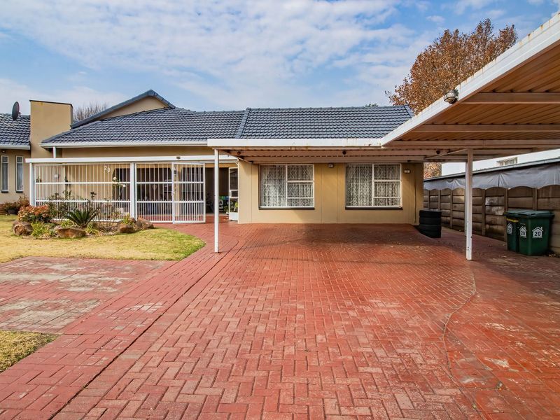 Front exterior view of the house featuring a paved driveway, a covered carport, and secure gated access to the main entrance.