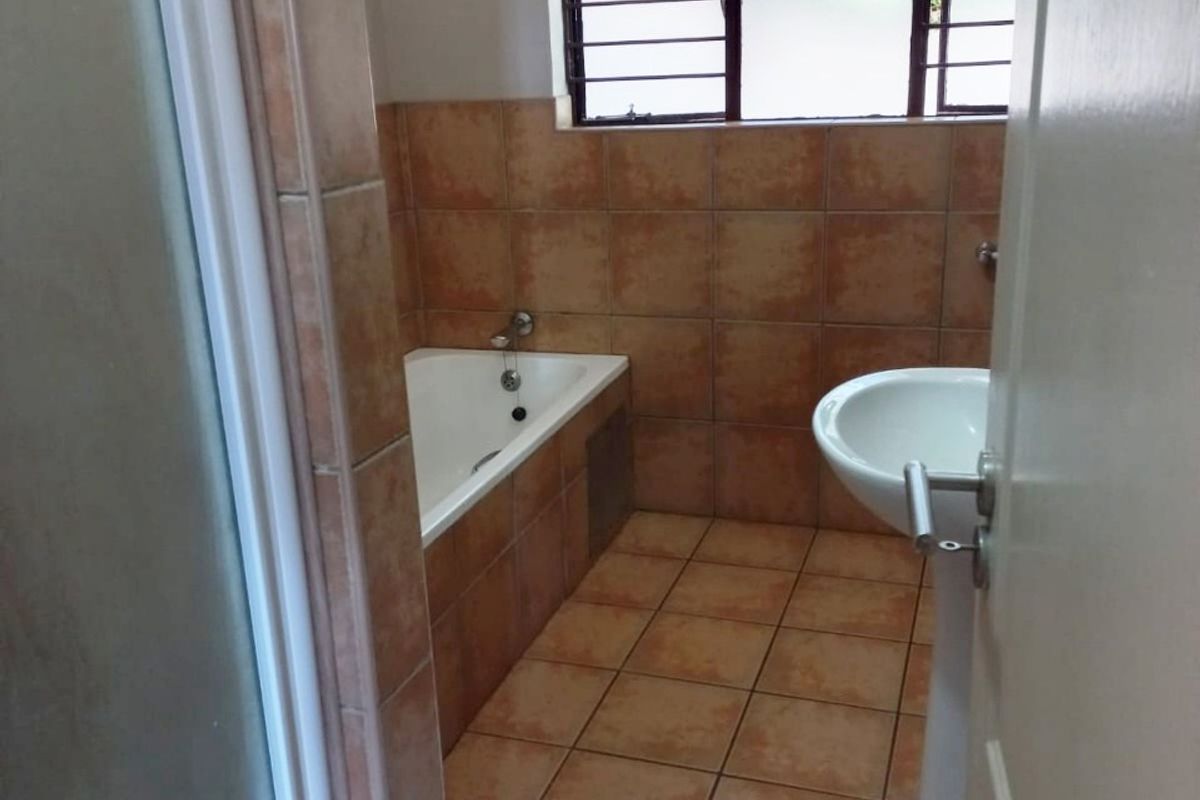 A functional bathroom featuring a built-in bathtub, pedestal basin, and separate shower enclosure with neutral tiled finishes.