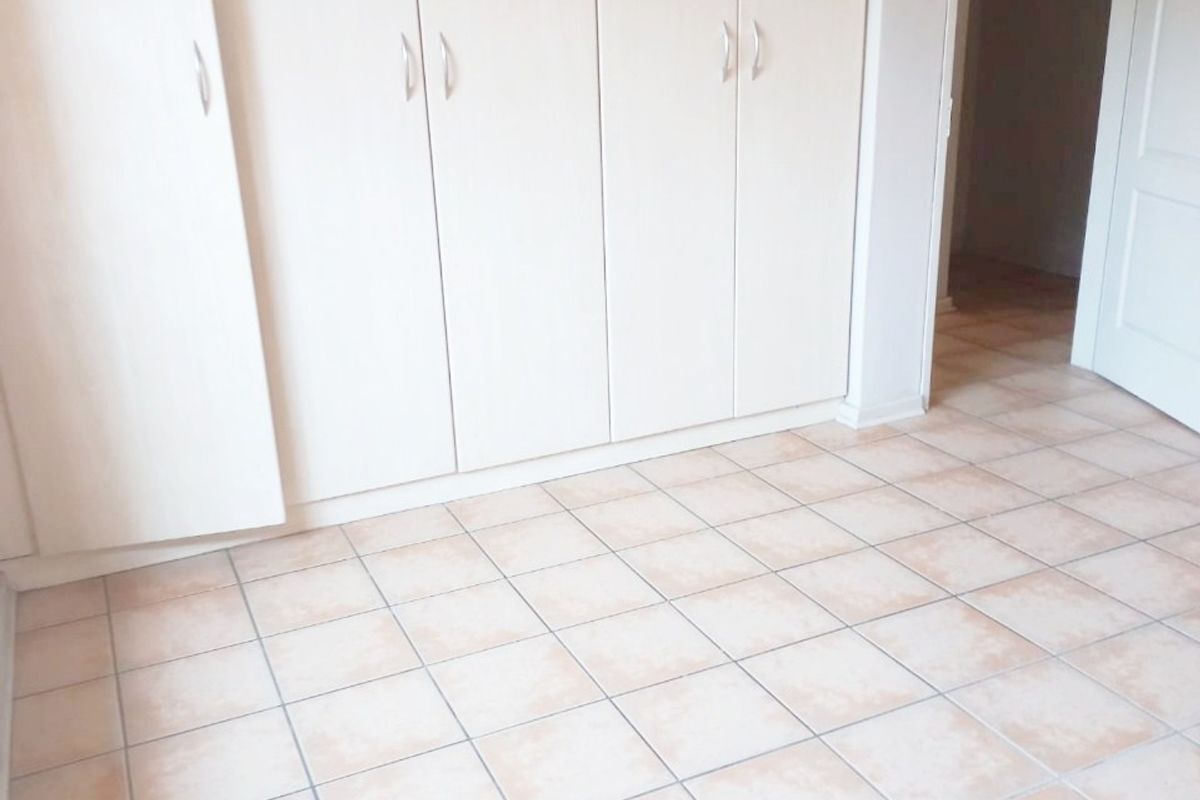 A bright, empty bedroom featuring neutral tiled flooring and ample built-in cupboard storage space.