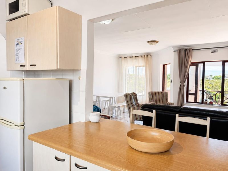 Open plan kitchen and living area featuring light wood cabinetry, laminate countertops, and direct access to a balcony through sliding glass doors.