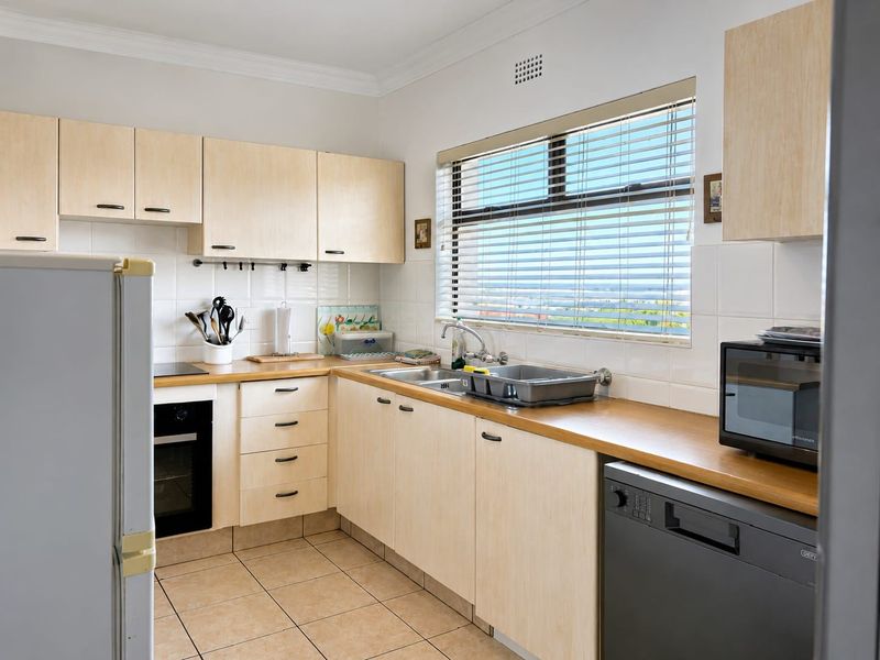 A functional kitchen featuring light wood cabinetry, wooden countertops, tiled backsplash, and integrated appliances, offering a clean and practical workspace.