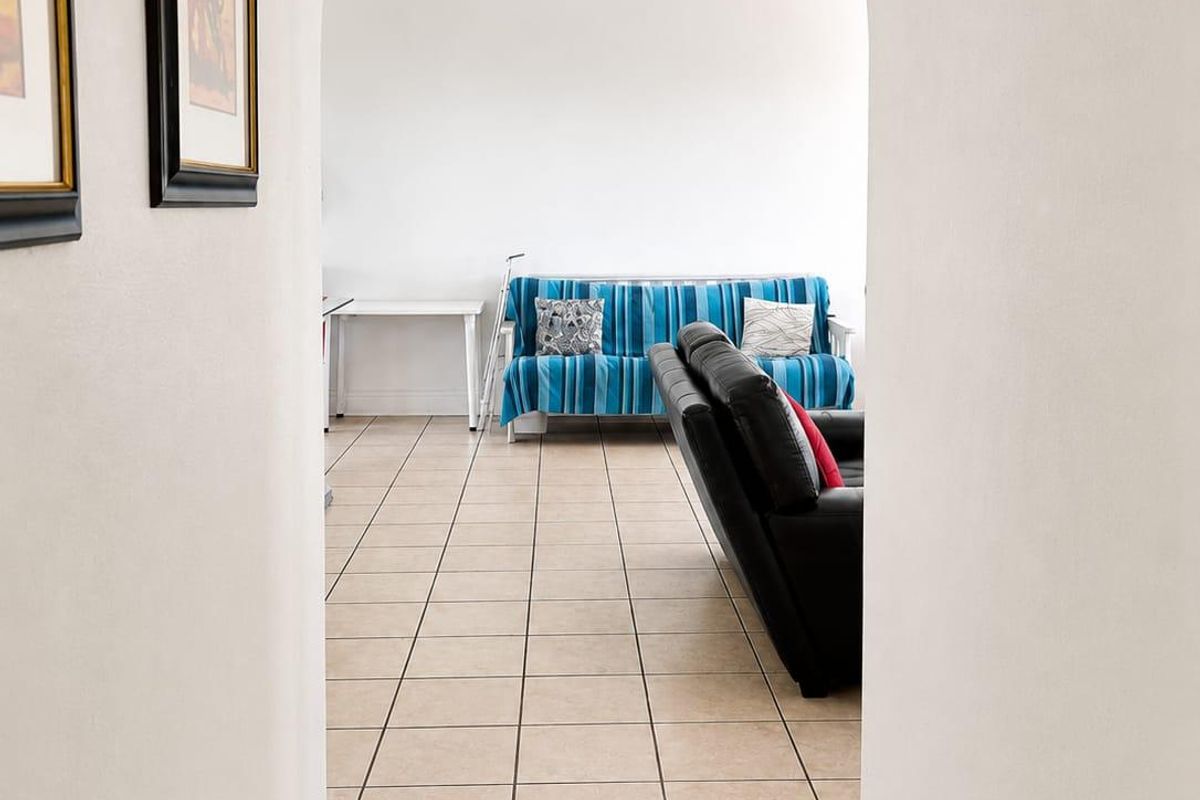 A view through an arched doorway into a living area featuring neutral tiled flooring and a simple ceiling light fixture.