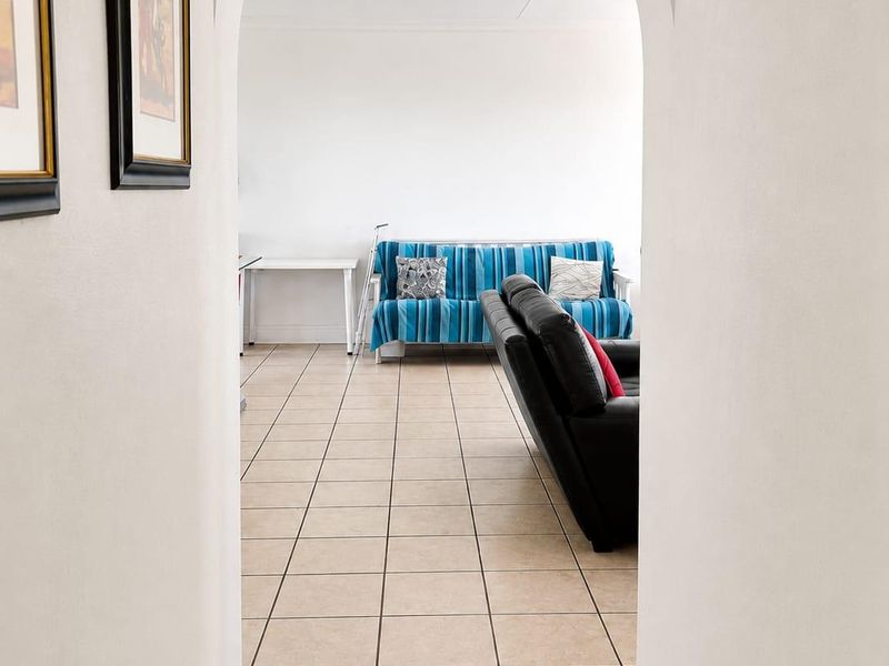 A view through an arched doorway into a living area featuring neutral tiled flooring and a simple ceiling light fixture.