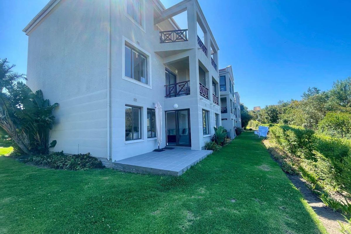 Rear view of the apartment building featuring a ground-floor tiled patio, upper-level balconies, and well-maintained surrounding lawn.