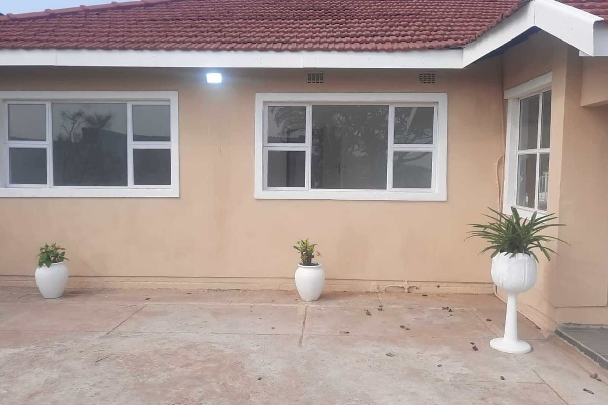 Rear exterior view of the house featuring a concrete patio area, white aluminium window frames, and a tiled roof.