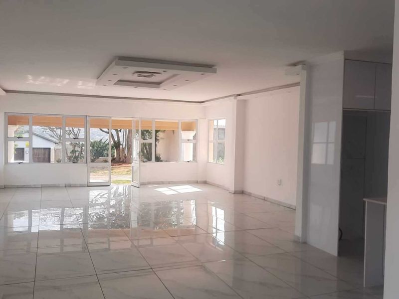 Spacious open-plan living area featuring polished porcelain floor tiles, a modern recessed ceiling design, and large glass sliding doors leading to the garden.