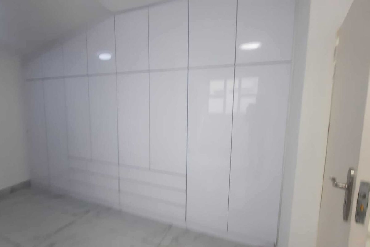 A clean, modern bedroom featuring floor-to-ceiling white built-in wardrobes with a high-gloss finish and integrated recessed lighting.