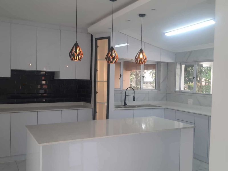 Modern, bright kitchen featuring white cabinetry, a central island with quartz countertops, dark subway tile backsplash, and contemporary pendant lighting.