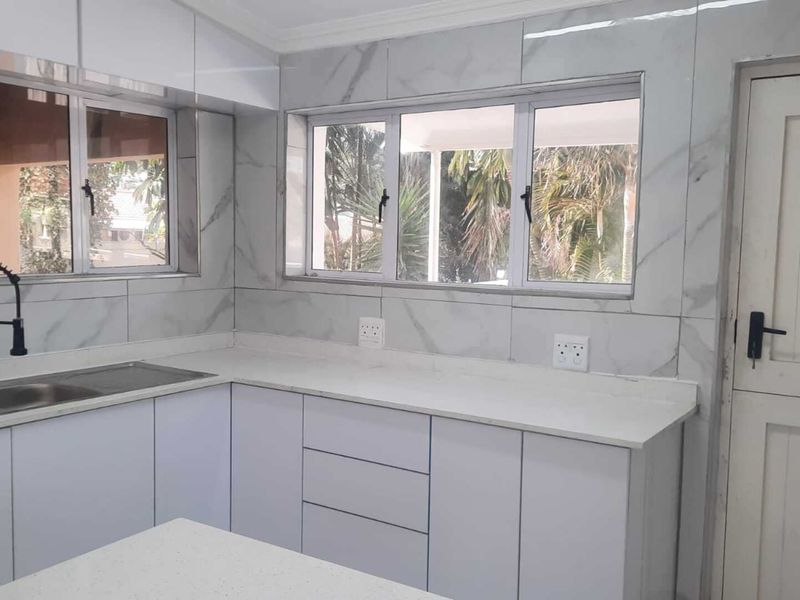 Modern kitchen featuring white cabinetry, quartz countertops, marble-look wall tiling, and a sleek gooseneck faucet with ample natural light.