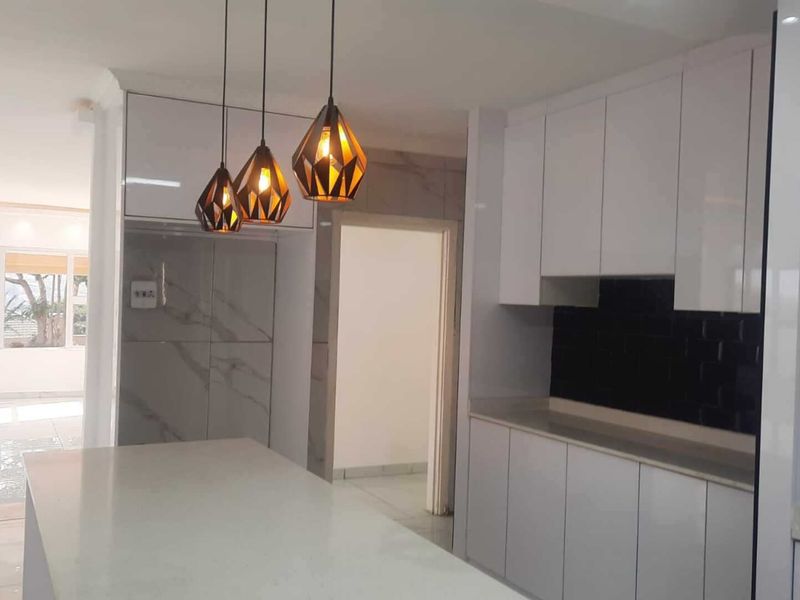 Modern kitchen featuring sleek white cabinetry, stone countertops, a dark tiled backsplash, and contemporary pendant lighting, offering a clean and minimalist aesthetic.