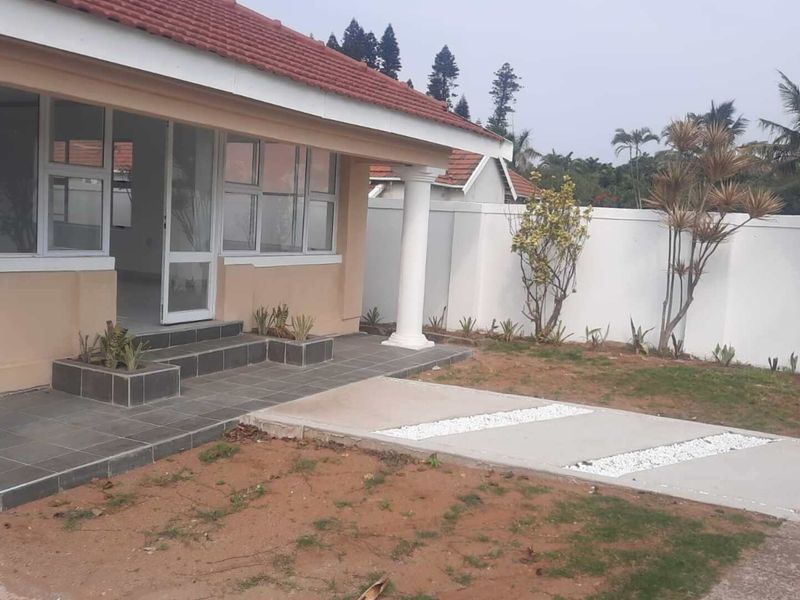 A rear exterior view of the house featuring a tiled patio with decorative columns, a perimeter wall, and a concrete pathway leading to the garden.