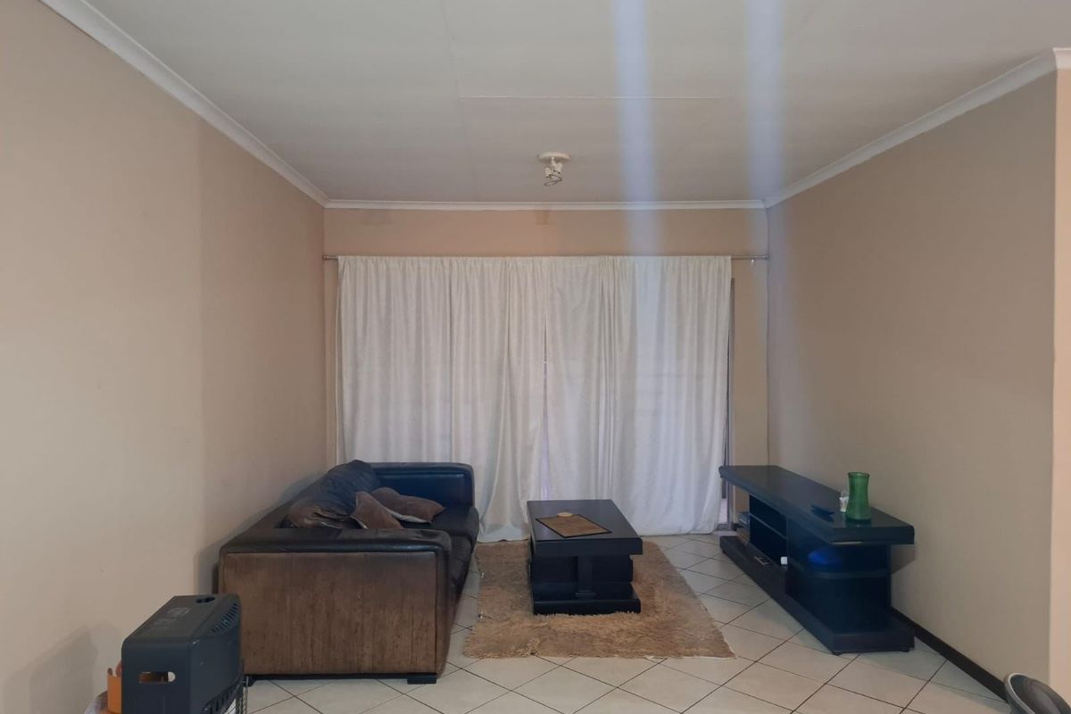 A living room featuring neutral wall paint, ceramic floor tiles, and a sliding glass door covered by curtains.