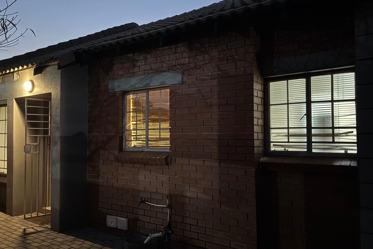 A view of the rear exterior facade featuring face brick construction, tiled roofing, and secure window bars at dusk.
