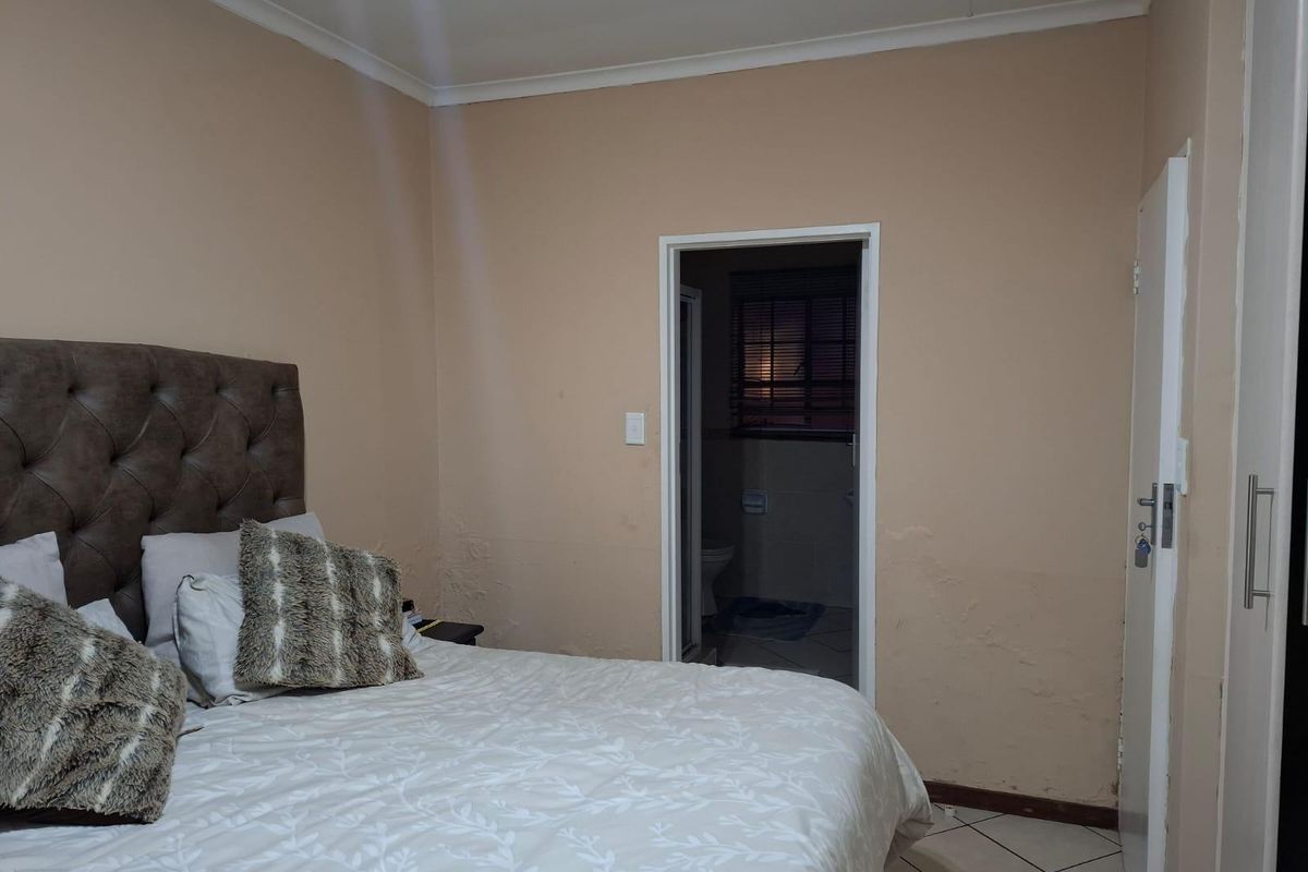 Bedroom featuring built-in cupboards and tiled flooring, with an adjoining bathroom. The walls show signs of surface wear and peeling paint.