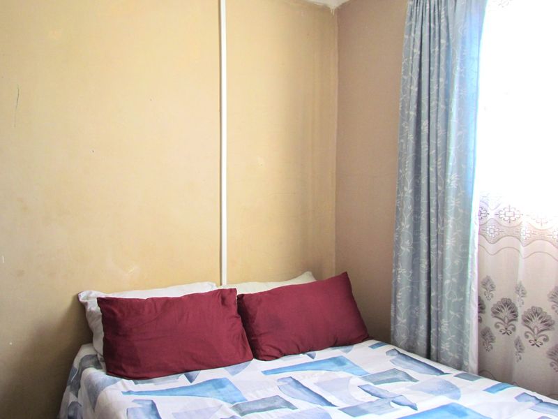 A compact bedroom featuring plain walls and a window with curtains, requiring cosmetic updates to improve the overall aesthetic.