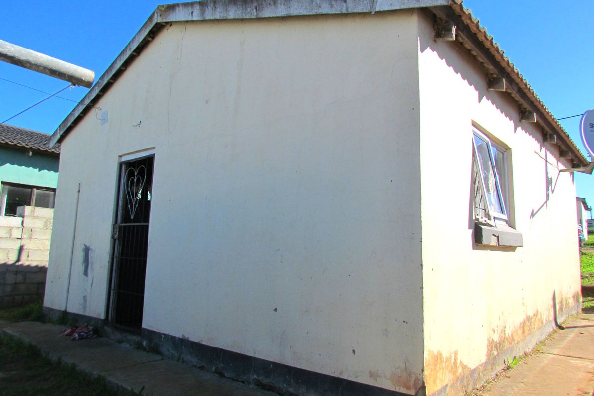 Rear view of a detached house showing exterior walls with visible signs of damp and weathering, a security gate, and a tiled roof.