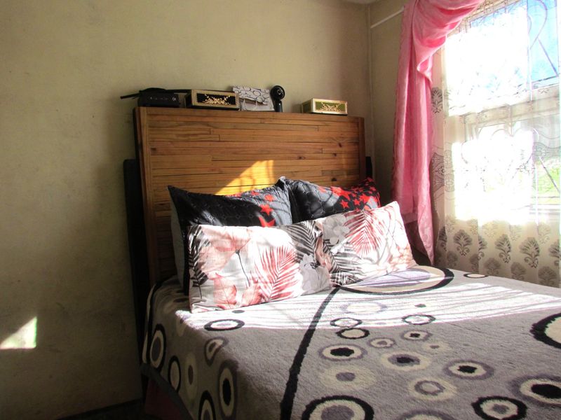 A bedroom featuring a window with security bars and natural light, requiring cosmetic updates to the wall finishes.