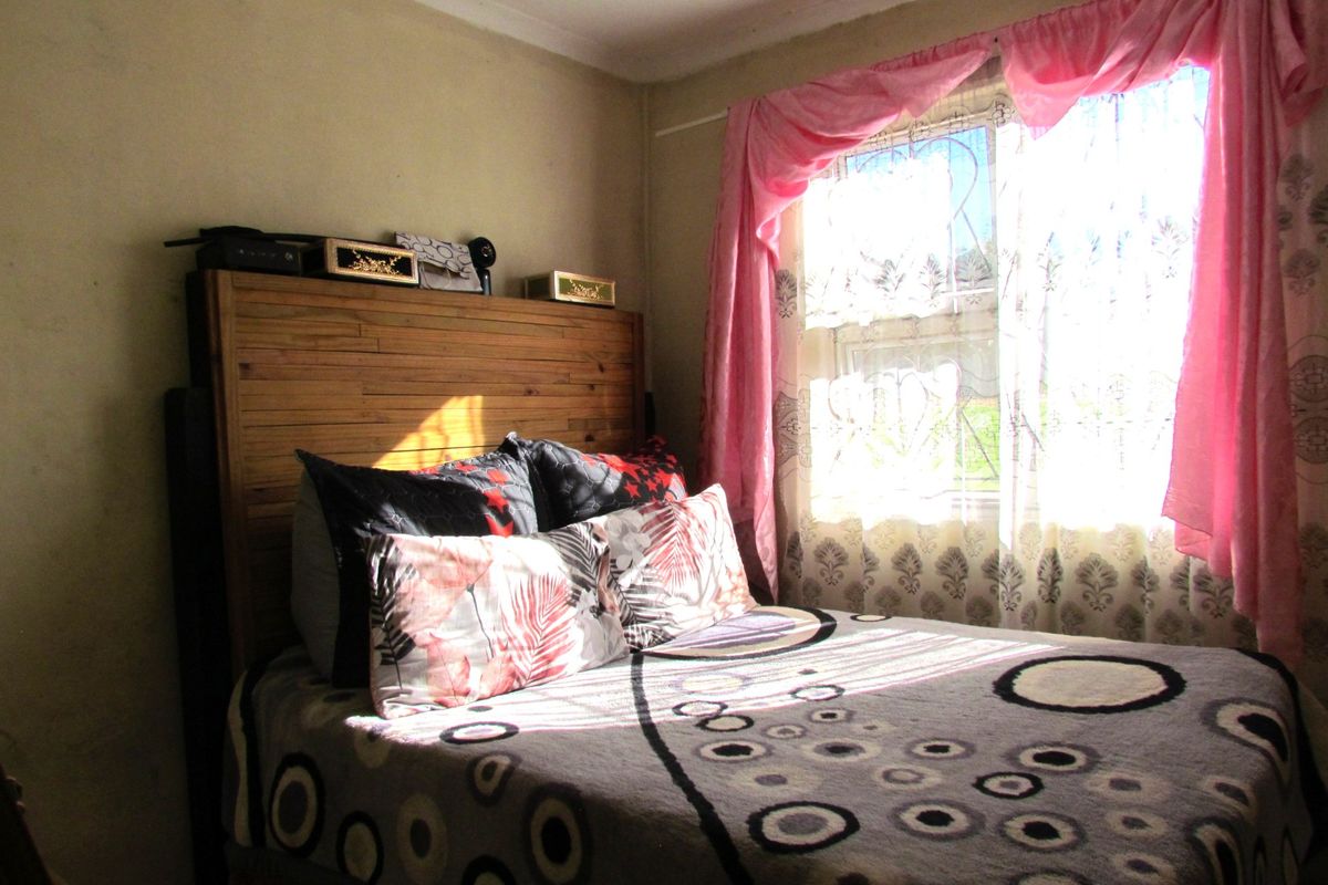 A bedroom featuring a window with security bars, requiring cosmetic updates to the wall finishes and ceiling cornices.