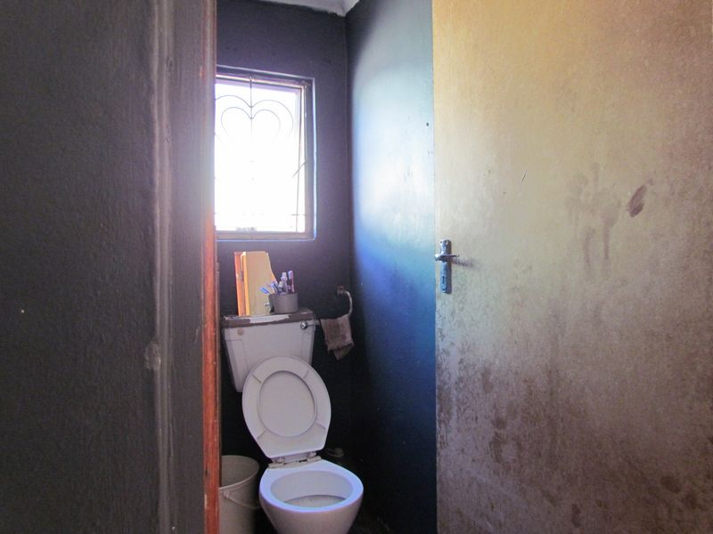 A small, dated bathroom featuring a standard toilet and a window with a security gate, requiring cosmetic updates to the walls and door.