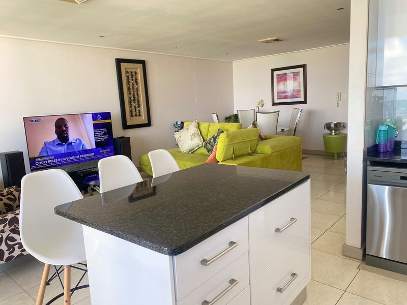 Open-plan living and kitchen area featuring a modern kitchen island with granite countertops, white cabinetry, and tiled flooring throughout.