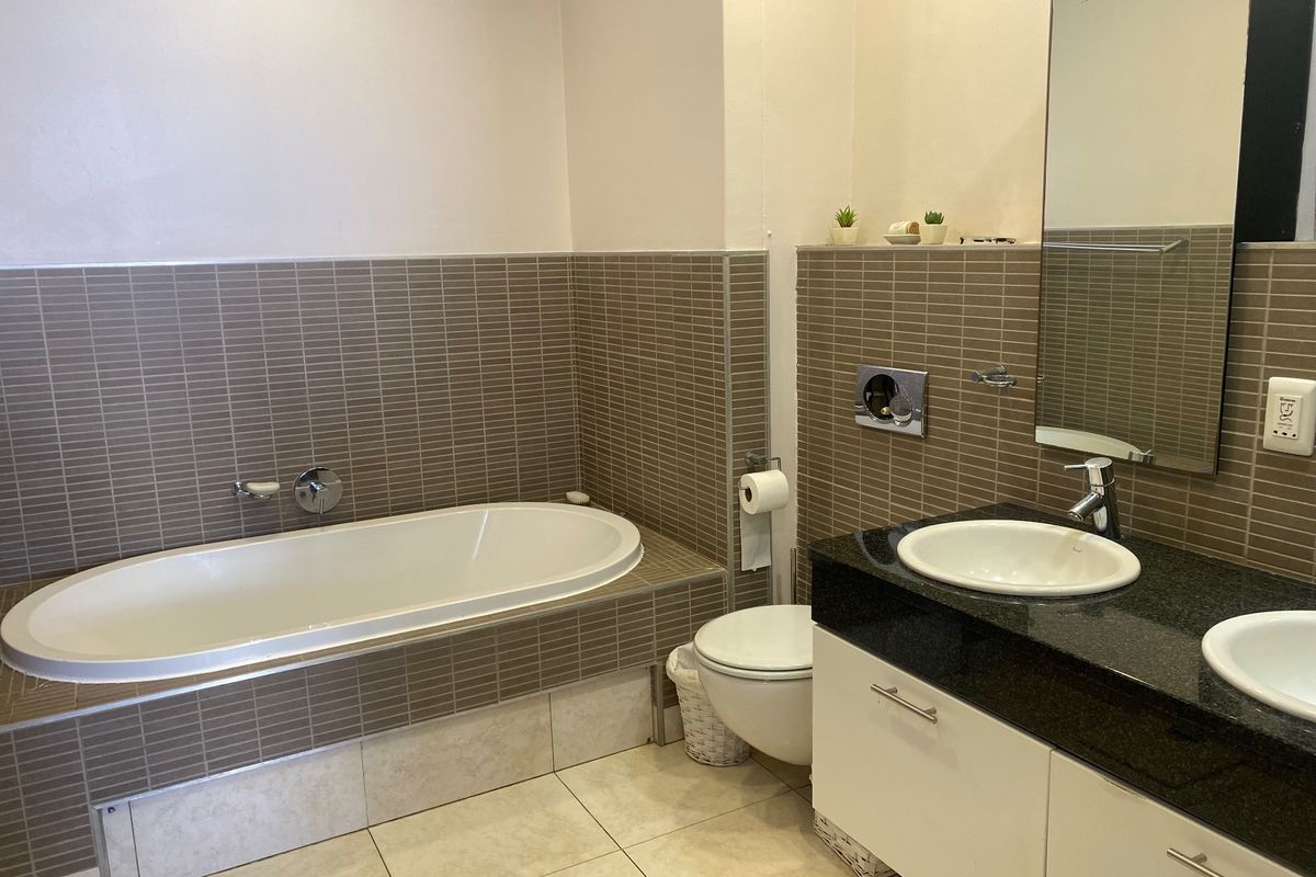 A functional bathroom featuring a built-in bathtub, wall-mounted toilet, and a double vanity with granite countertops and tiled wall finishes.