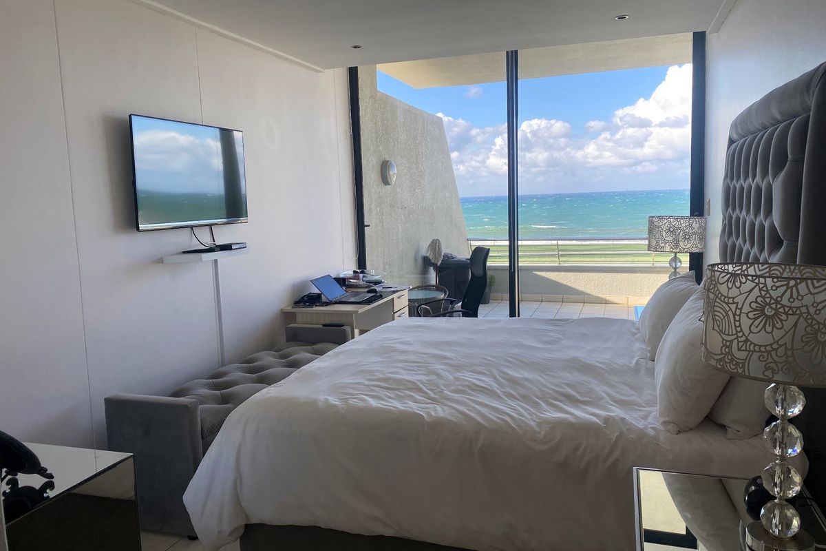 Spacious bedroom featuring large sliding glass doors that open onto a balcony with expansive ocean views and modern recessed lighting.
