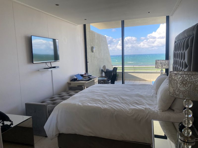 Spacious bedroom featuring large sliding glass doors that open onto a balcony with expansive ocean views and modern recessed lighting.