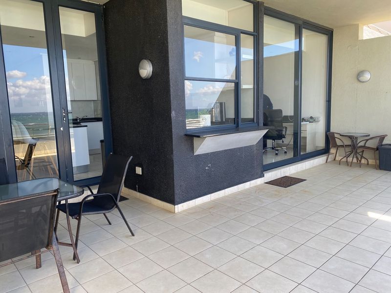 Spacious covered balcony featuring tiled flooring, large sliding glass doors providing access to interior living spaces, and exterior wall lighting.