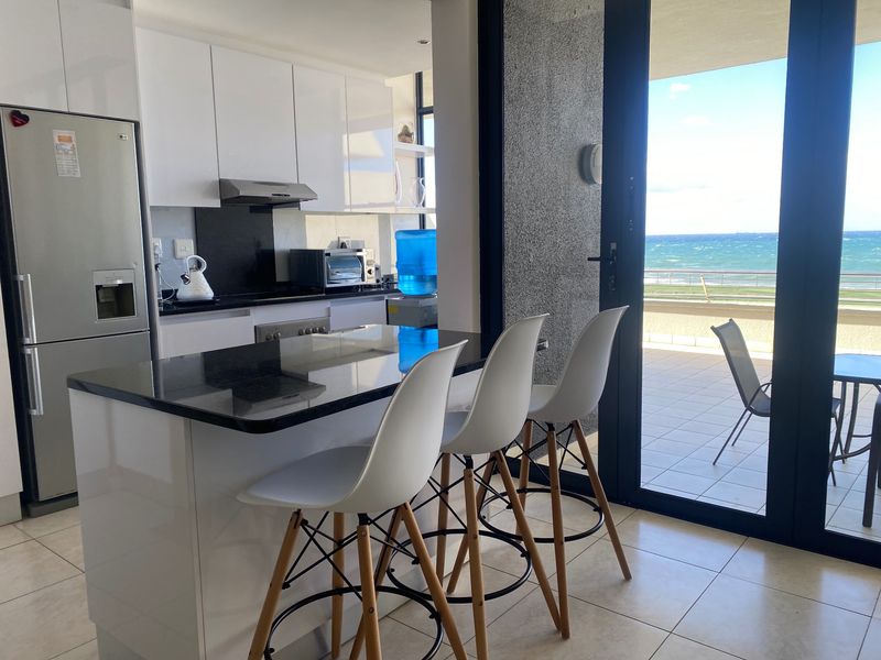 Modern open-plan kitchen featuring sleek white cabinetry, granite countertops, and direct access to a balcony with scenic ocean views.