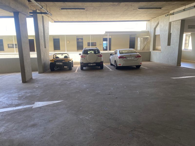 A covered parking garage area featuring concrete structural columns, overhead lighting, and marked parking bays within an apartment complex.