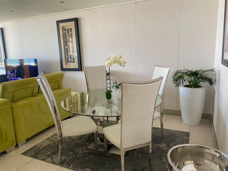 An open-plan living and dining area featuring neutral tiled flooring and recessed ceiling lighting, providing a bright and functional space.