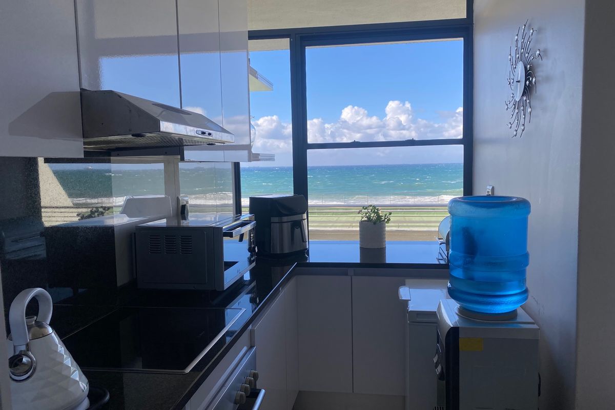 Modern kitchen featuring sleek white cabinetry, black granite countertops, and integrated appliances, complemented by a stunning direct ocean view.