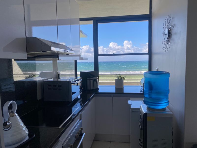 Modern kitchen featuring sleek white cabinetry, black granite countertops, and integrated appliances, complemented by a stunning direct ocean view.