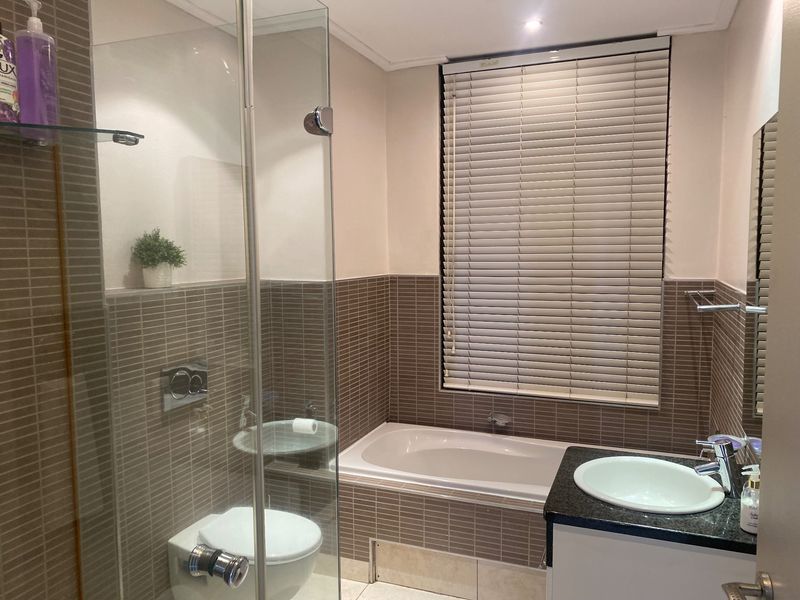 A well-maintained bathroom featuring a glass-enclosed shower, a built-in bathtub, a wall-mounted toilet, and a vanity basin with tiled wall finishes.
