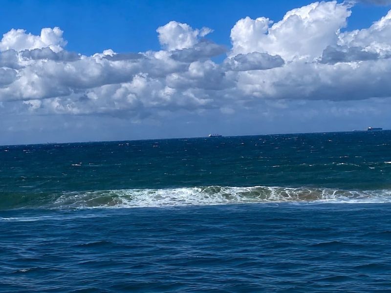 A scenic view of the open ocean with waves and a cloudy blue sky.