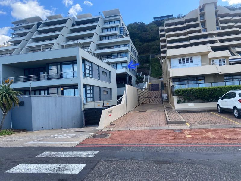 Front exterior view of a modern apartment complex featuring a paved driveway, secure gated entrance, and multi-level balconies.