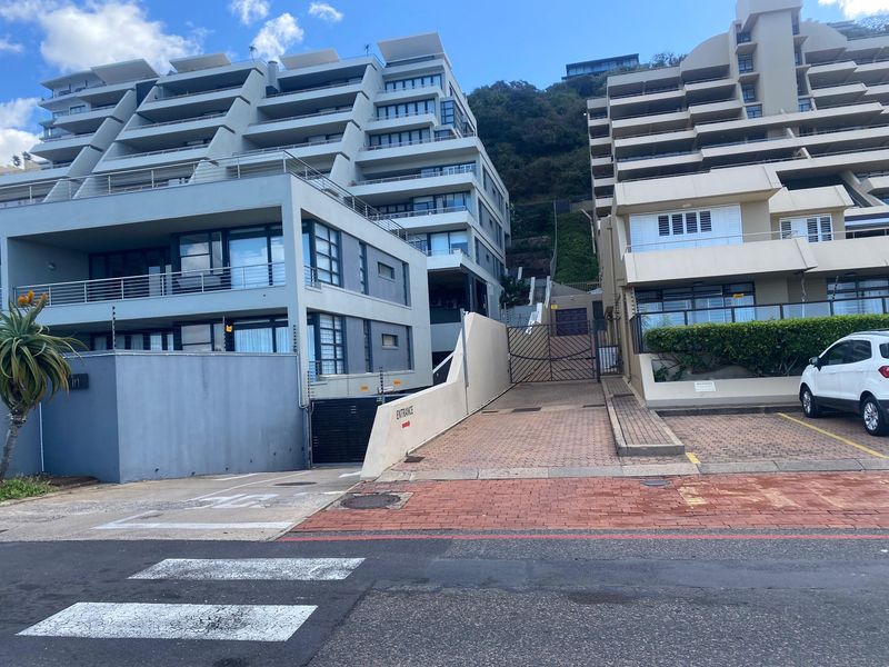 Front exterior view of a multi-story apartment complex featuring a paved driveway, secure gated entrance, and tiered balconies.