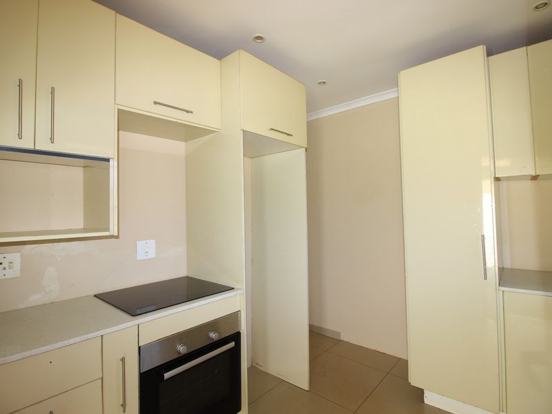 A functional kitchen featuring cream-colored built-in cabinetry, an integrated electric hob and oven, tiled flooring, and recessed lighting.
