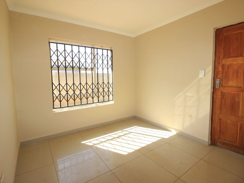 A clean, empty bedroom featuring neutral tiled flooring, a wooden door, and a window fitted with a security gate.