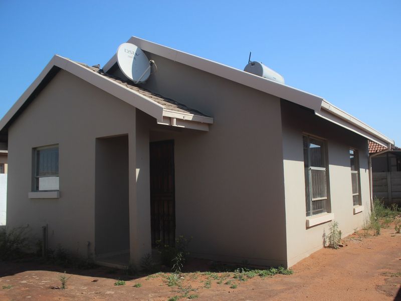 Front exterior view of a single-story house featuring a tiled roof, solar geyser, satellite dish, and security gate entrance.