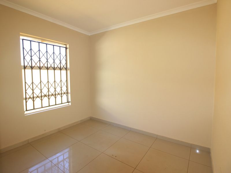 A clean, empty bedroom featuring neutral wall paint, tiled flooring, and a window fitted with a security gate.