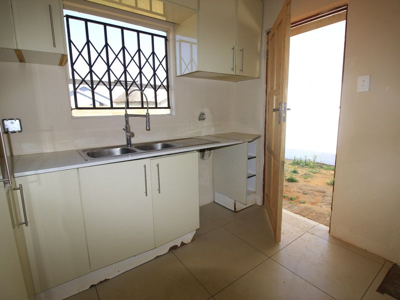 A compact kitchen featuring built-in cabinetry, a stainless steel sink, and direct access to the exterior, requiring some cosmetic repairs and finishing touches.